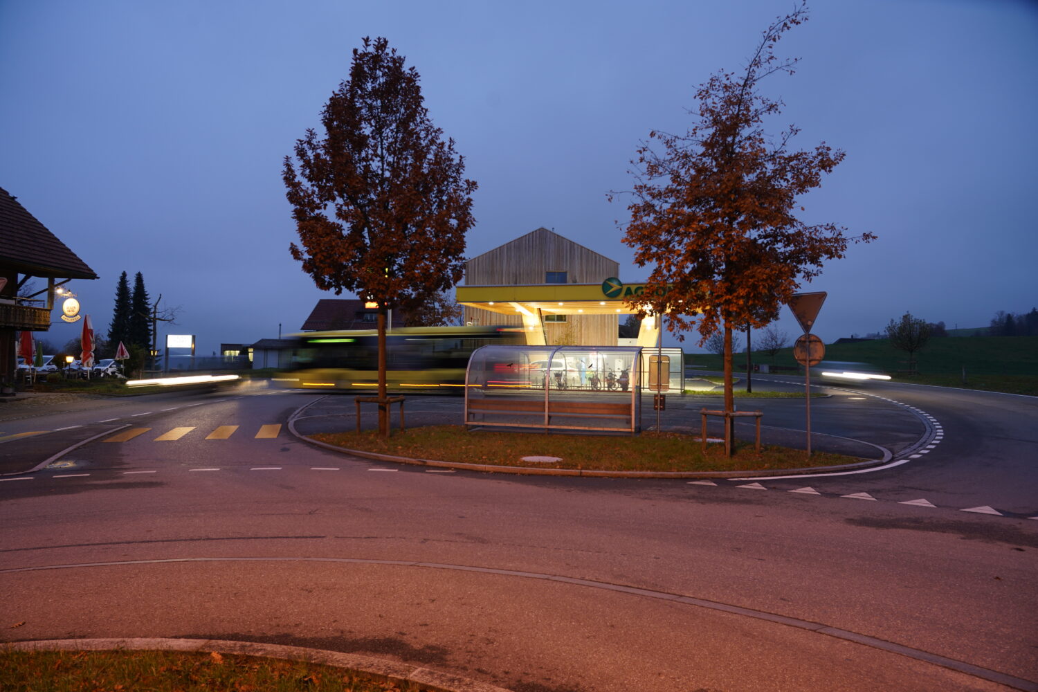 Abendaufnahme mit Bushaltestelle und Tankstelle im Vordergrund